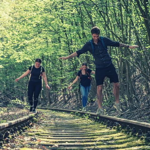 Drei Wanderer balancieren auf stillgelegten Bahntrassen in einem Lost Place im Gamengrund 